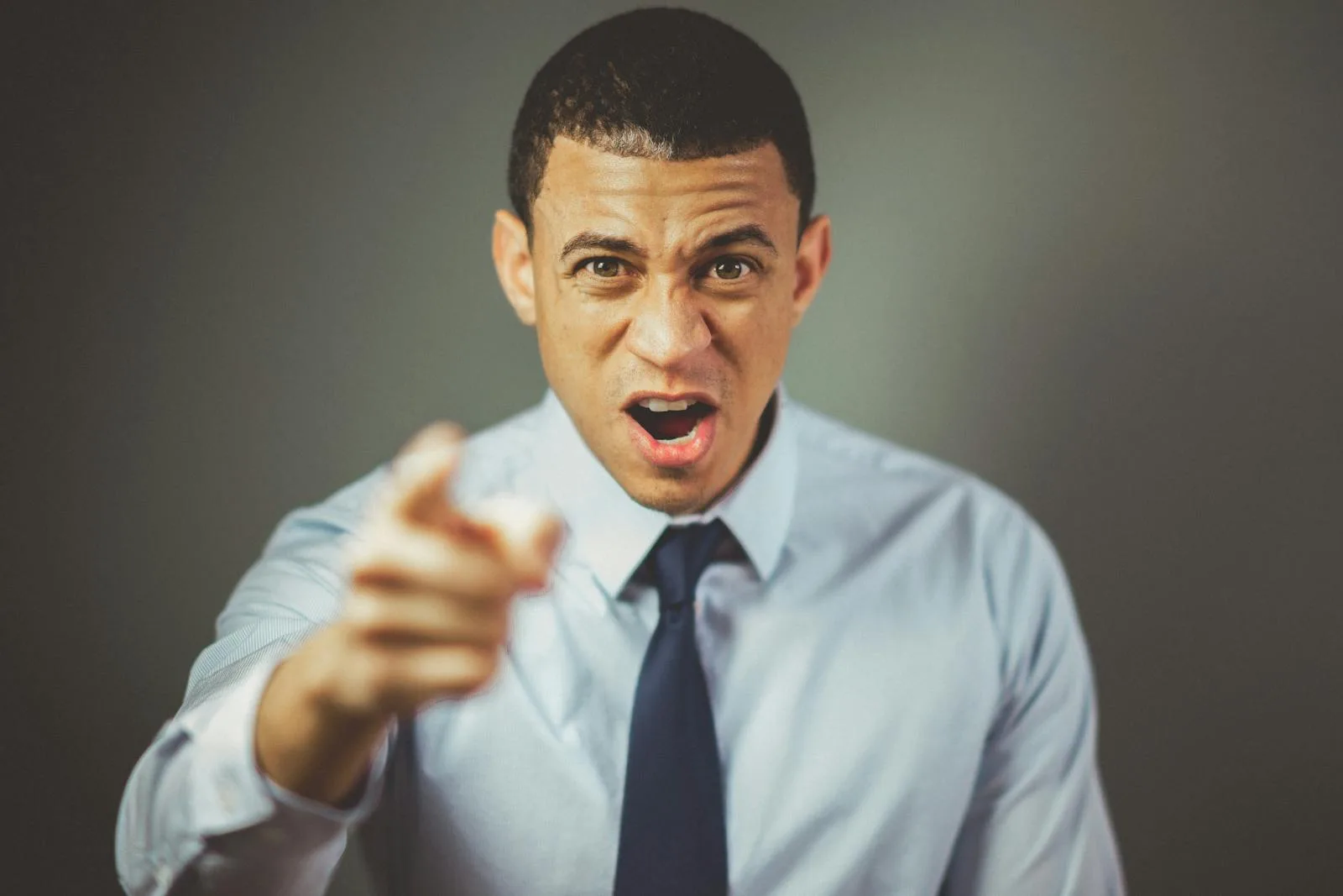 Close-up of an angry businessman in a tie expressing frustration and pointing.