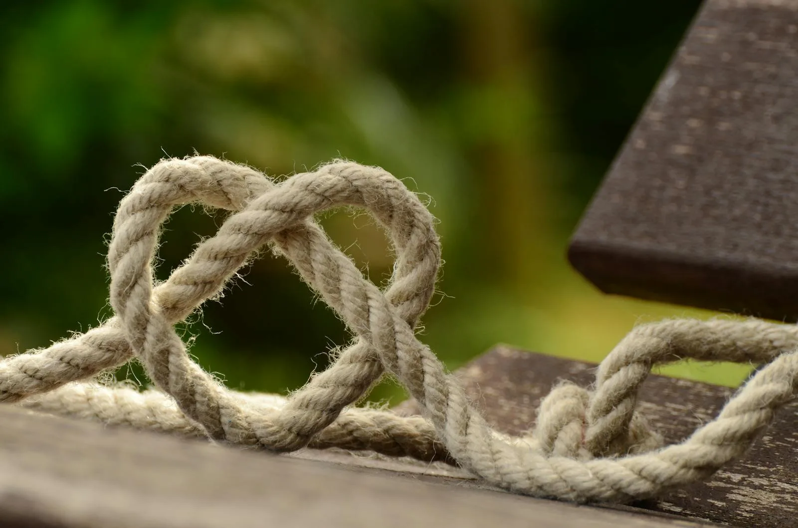 Close-up of twine forming a heart shape on a rustic wooden table outdoors.