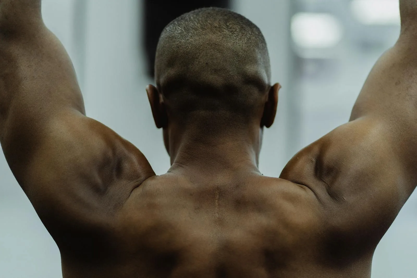 Shirtless man showing strength with visible muscles during workout, focus on back view.