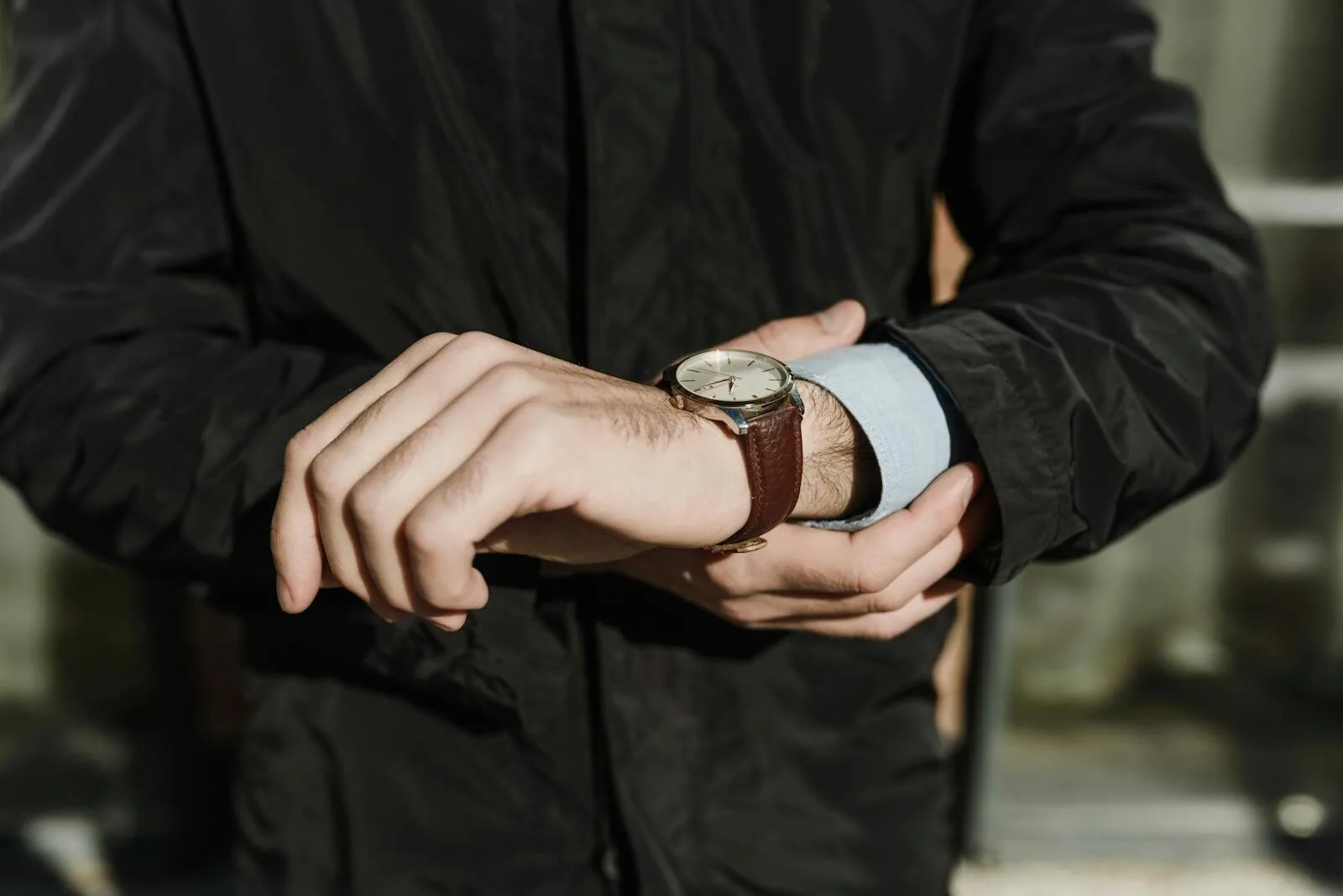 Close-up of a man's hands adjusting a classic leather watch outdoors.