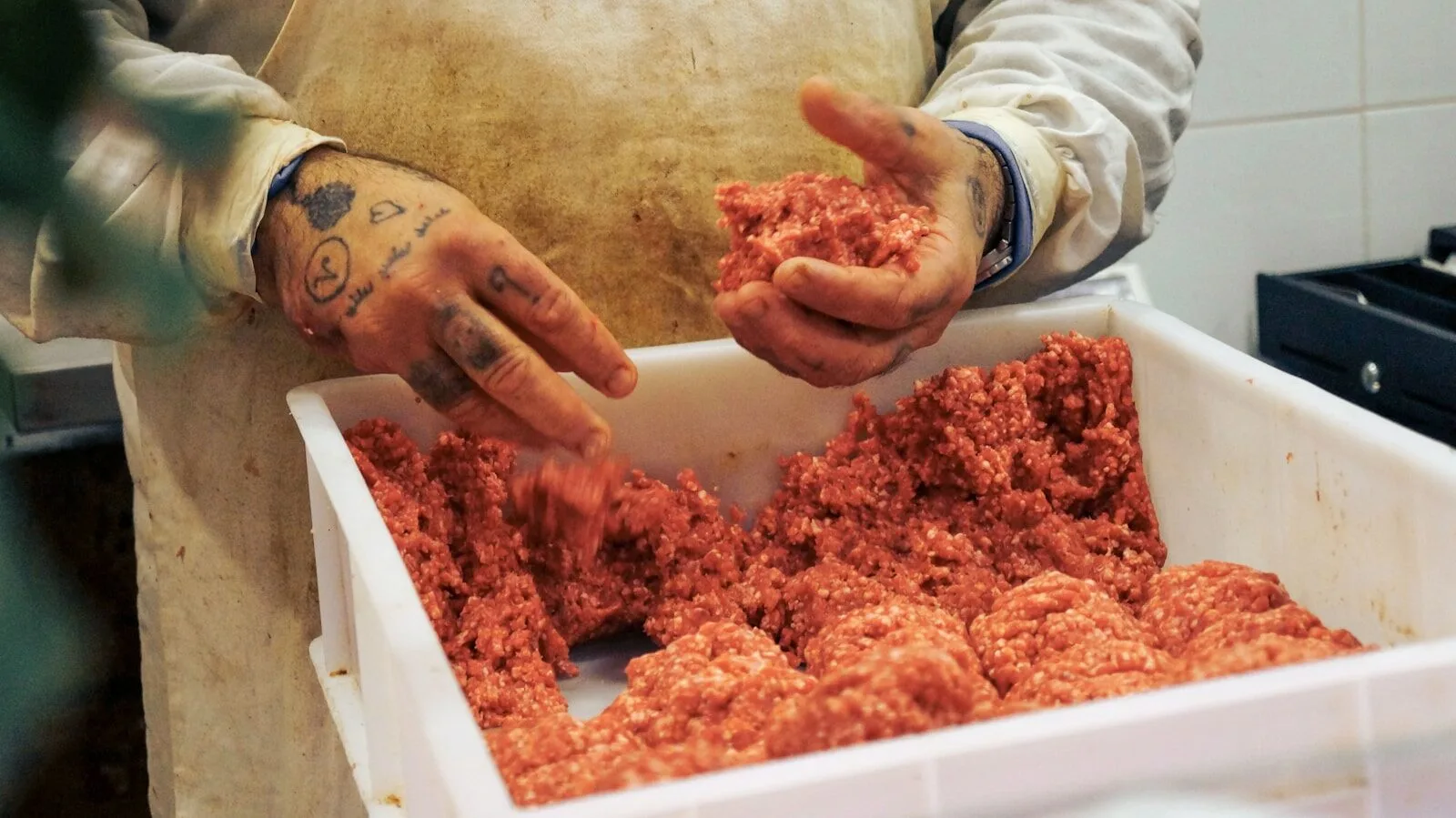 Butcher hands are shaping raw, ground meat.