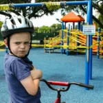 boy in blue denim vest and helmet riding red bicycle