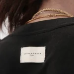 Person wearing black shirt, white label, and gold necklaces.