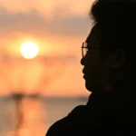 Man in silhouette watches the sunset over the ocean.
